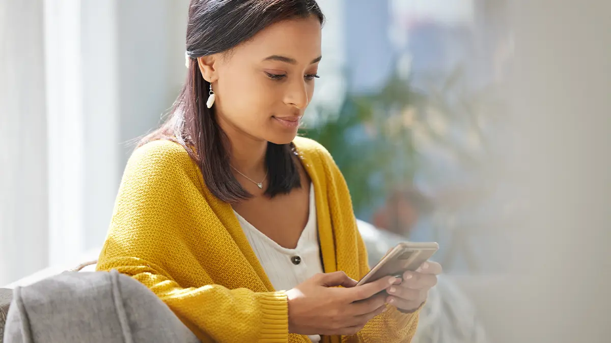 Woman sitting on couch while looking at phone.